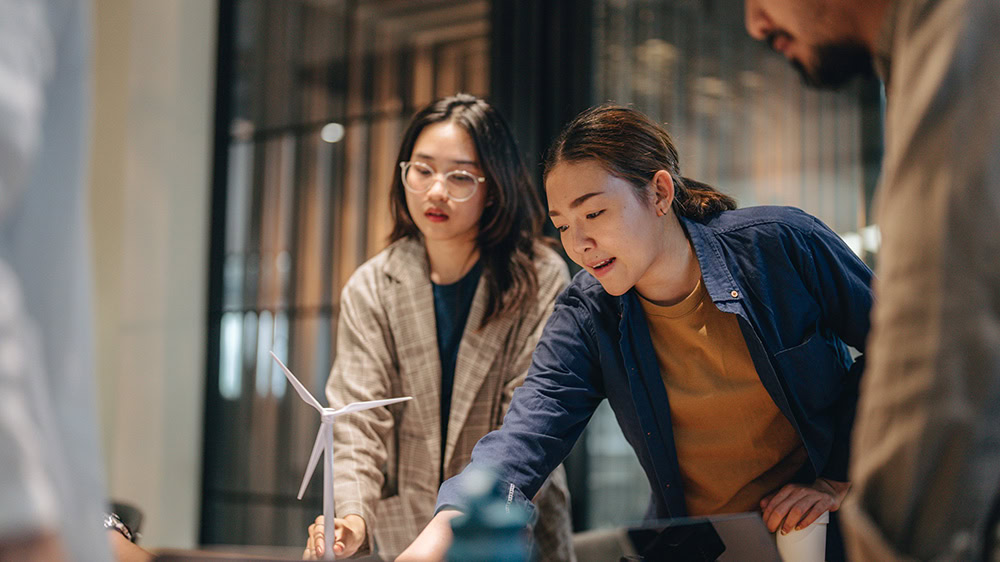 Team of students standing around a meeting table discussing a project. 