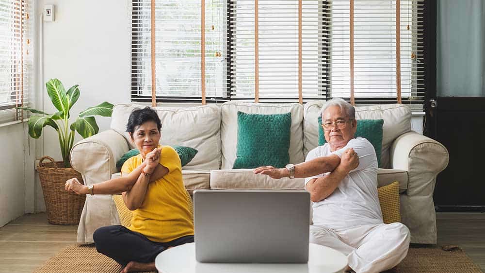 Couple doing yoga stretches and watching a laptop at home