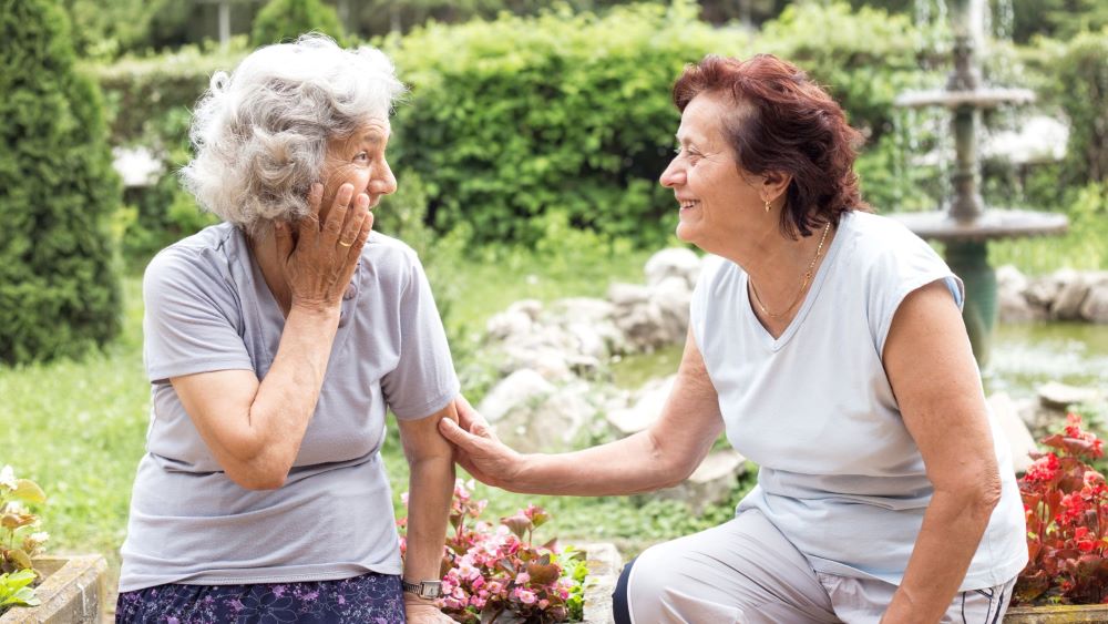 Two ladies sitting down in a garden, talking to each other