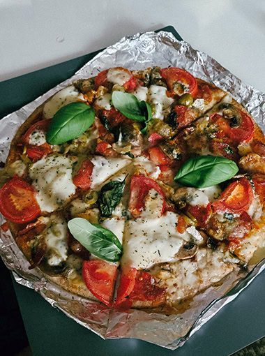 Homemade pizza with melted cheese, tomatoes, olives, mushrooms, and fresh basil leaves.