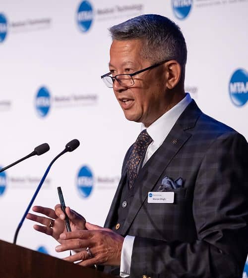 Headshot of Warren Bingham standing at podium giving speech