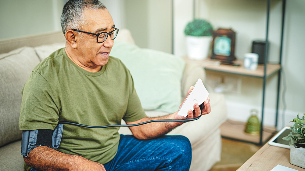 older man in a green tshirt measuring blood pressure at home
