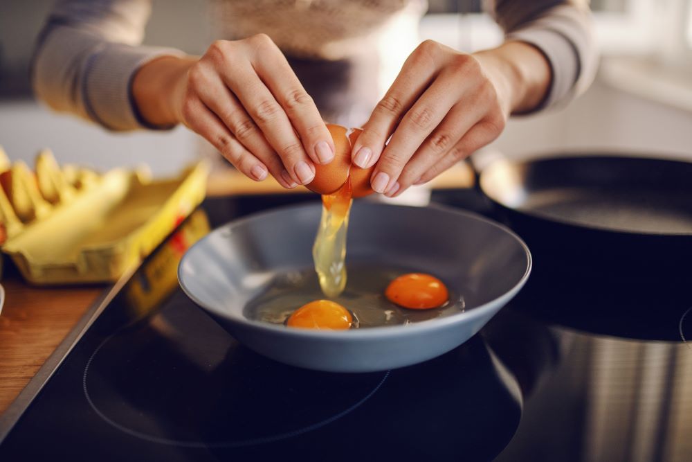 Woman in kitchen making breakfast, breaking egg into pan